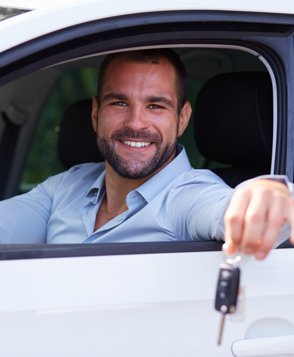 Ein lächelnder Mann schaut aus einem weißen Wagen und hält dabei Autschlüssel in der Hand