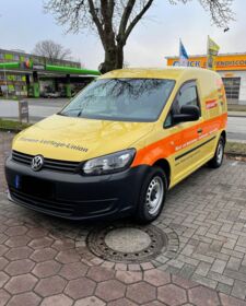 Ein gelber VW Caddy Firmenwagen steht auf einem Parkplatz