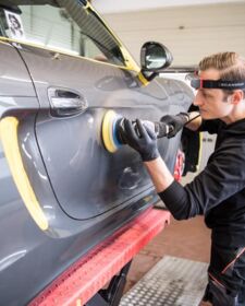 Mitarbeiter poliert graues Auto auf einer Hebebühne