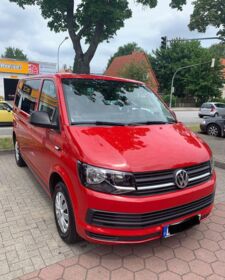 Ein roter Volkswagen T6 steht frontal auf einem Parkplatz