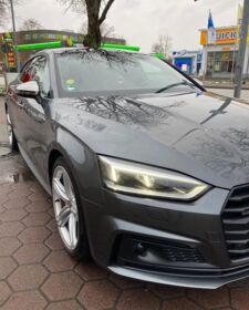 Ein dunkelgrauer Audi A5 Sportback steht auf einem Parkplatz