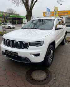 Ein weißer Jeep Grand Cherokee steht auf einem Parkplatz